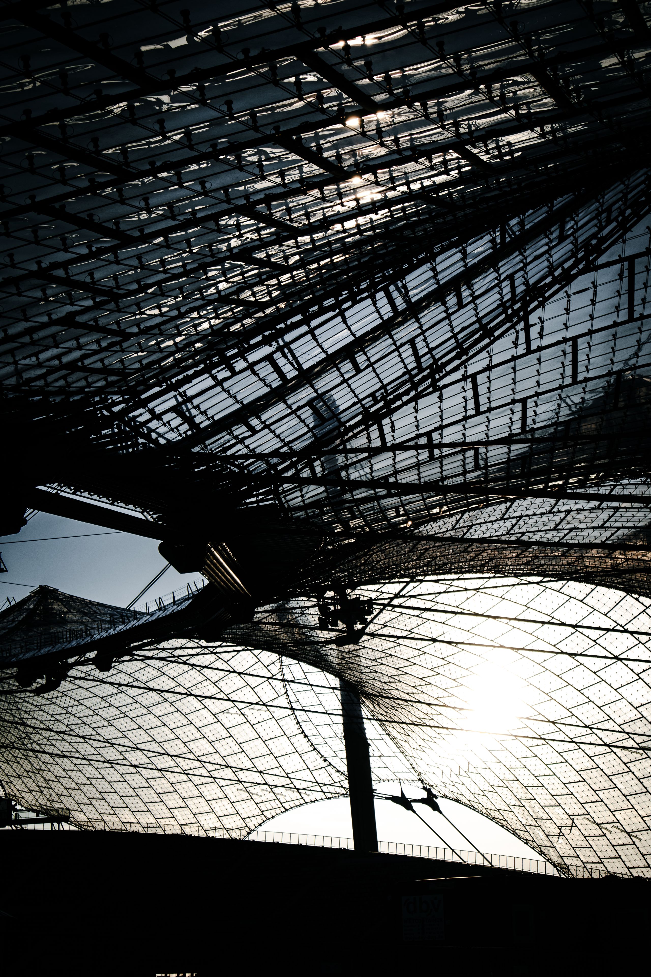 A complex structure of overlapping metal grids with sunlight filtering through, creating intricate patterns and shadows