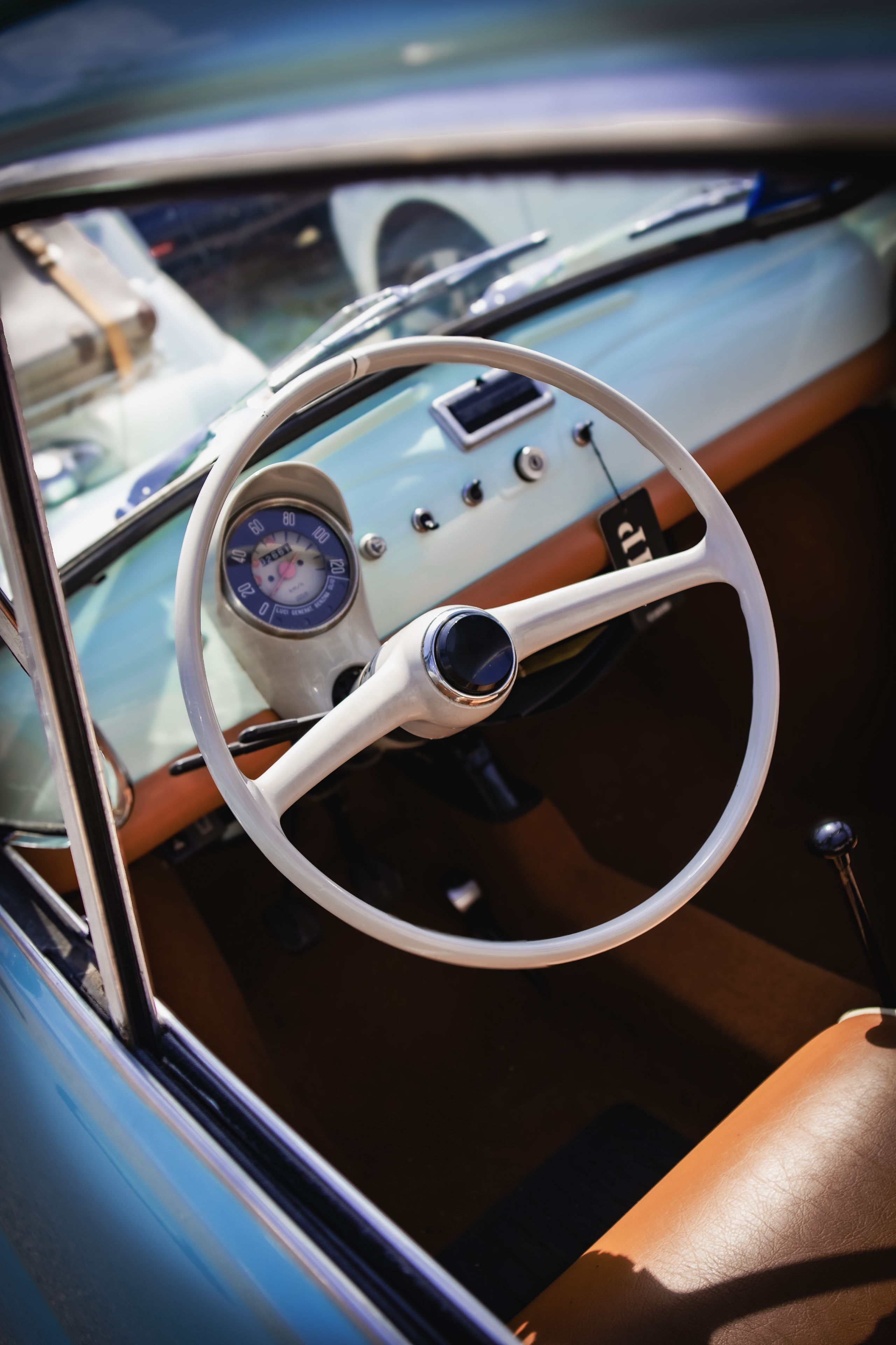 A vintage car interior featuring a white steering wheel, a classic speedometer, and brown upholstery