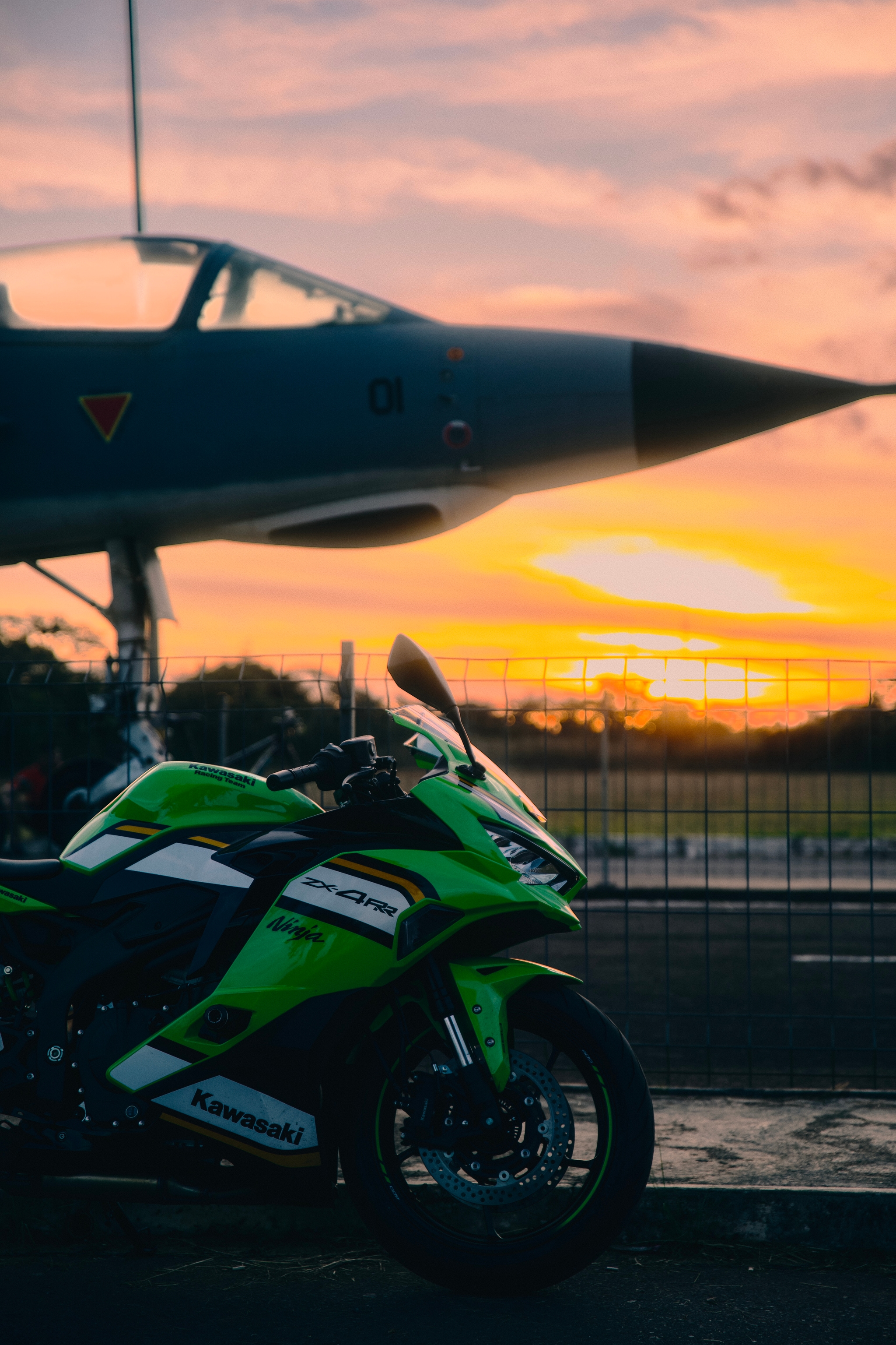 Green motorcycle parked in front of a jet at sunset