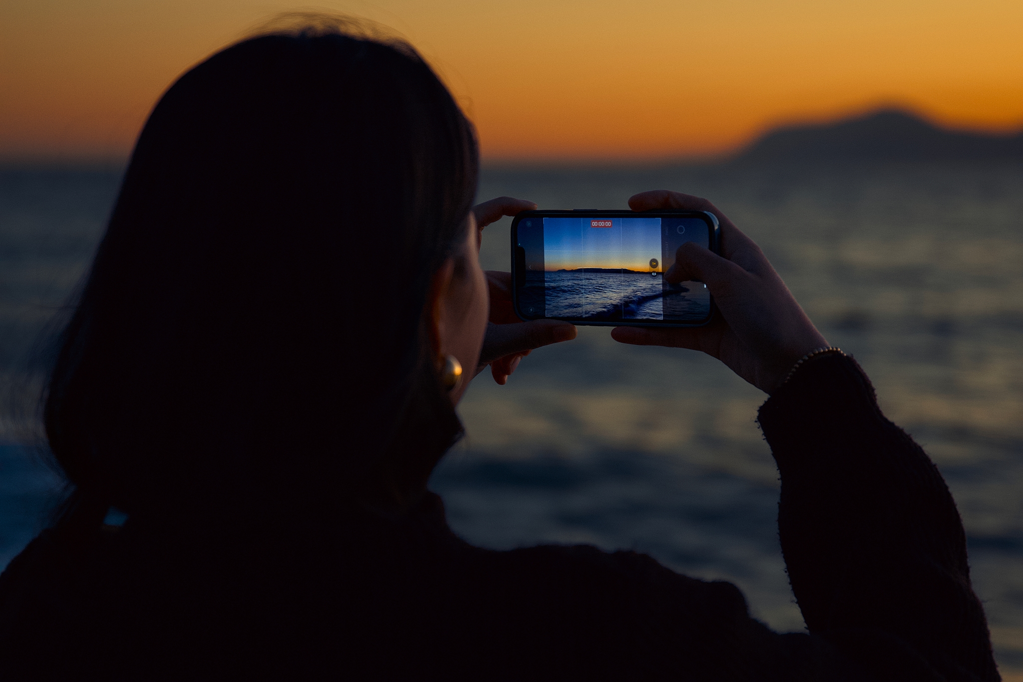 A person taking a video of a sunset over the ocean with a smartphone