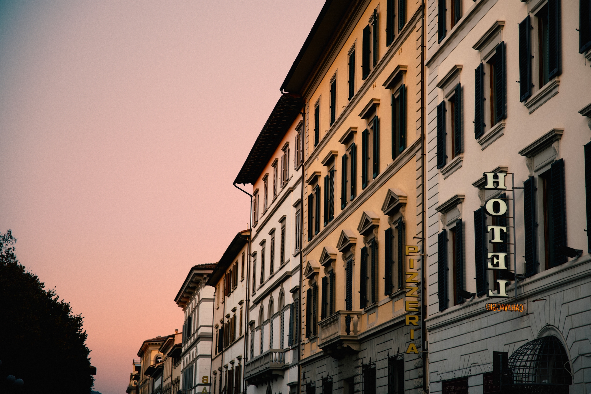 Low-angle view of a multi-story hotel building along a street at dusk with a warm sunset glow