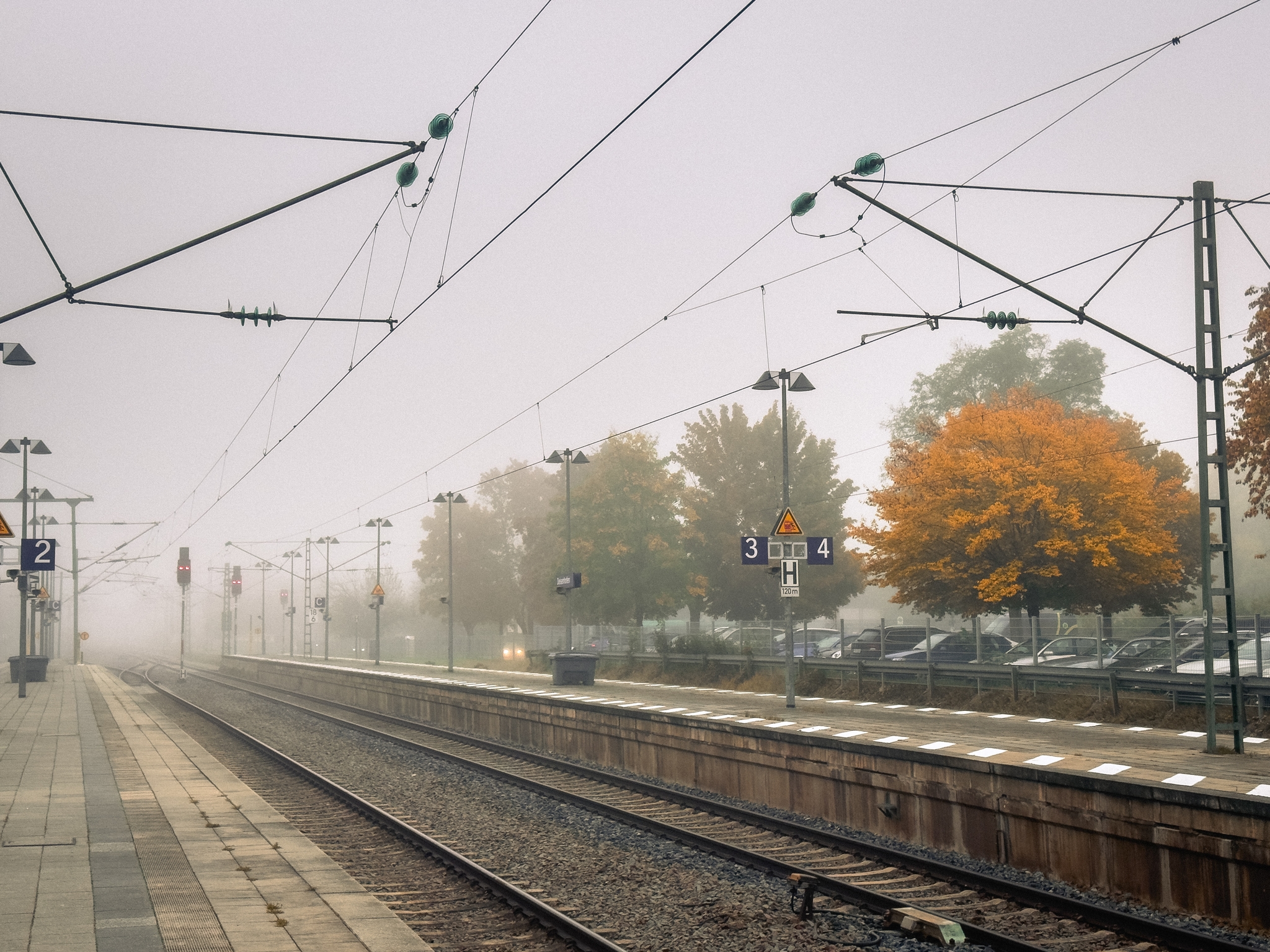Empty train platform with overhead wires and autumn trees in foggy weather