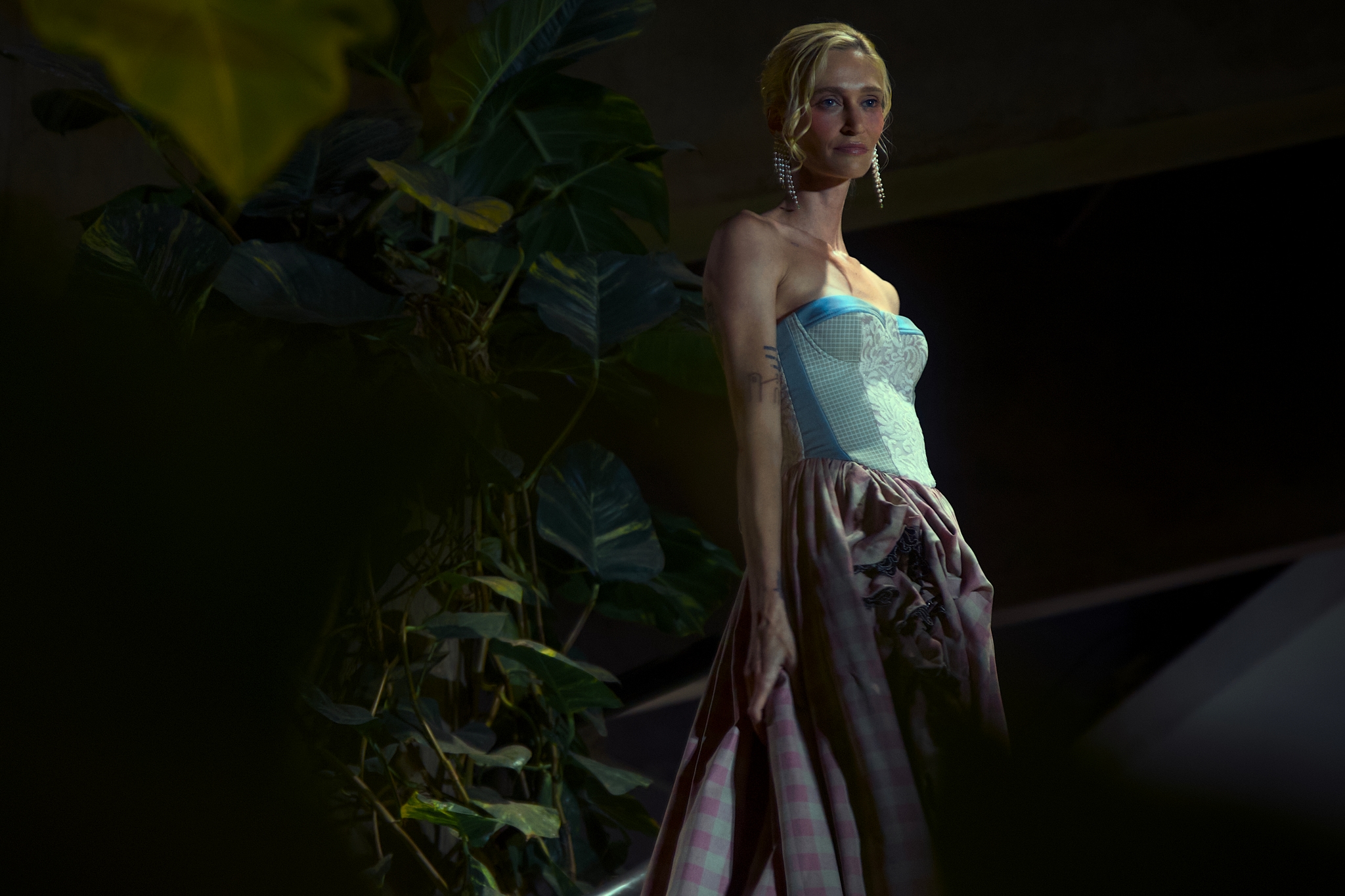 Woman in a strapless gown standing by dense foliage in low light