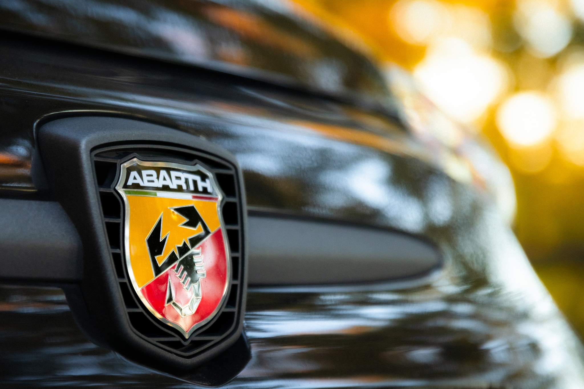 Close-up of the Abarth logo on a car grille, with blurred autumn foliage in the background