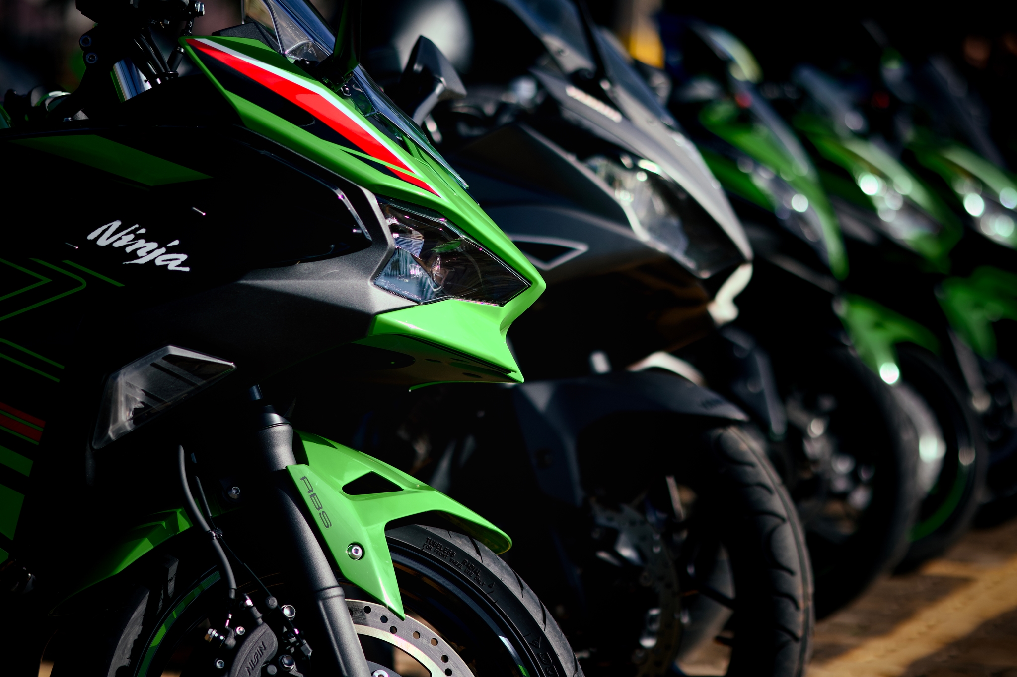 A row of green and black sport motorcycles parked closely together, with a focus on the front sections
