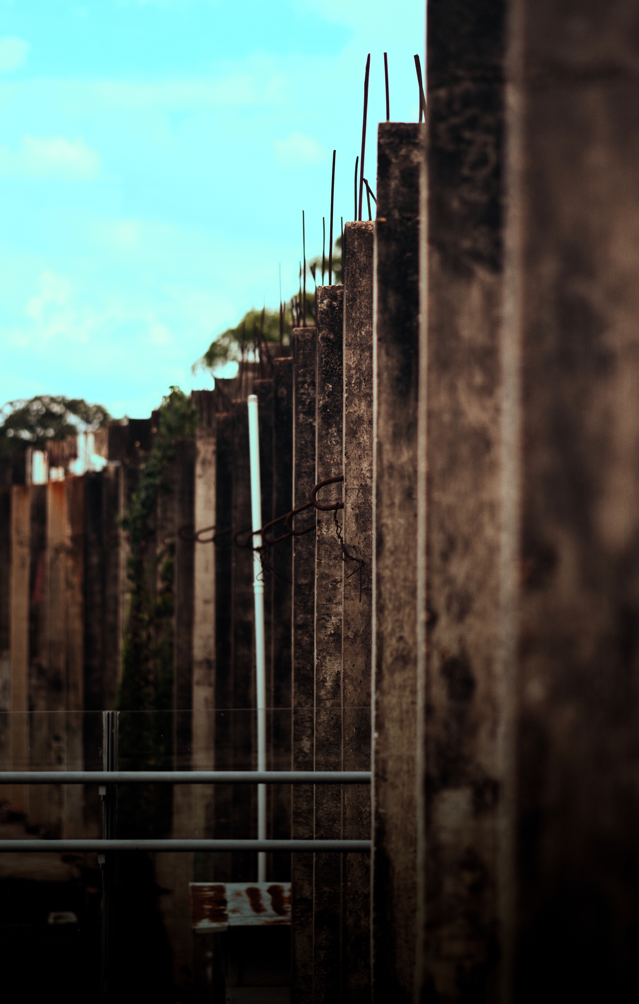 A row of weathered concrete pillars with exposed rebar, set against a blue sky