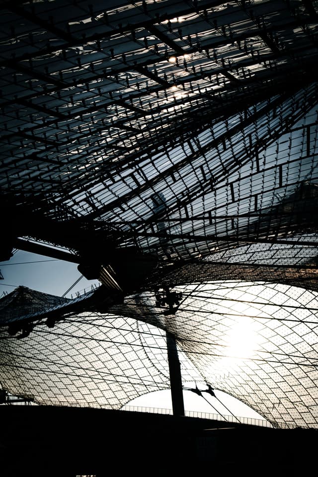 A complex structure of overlapping metal grids with sunlight filtering through, creating intricate patterns and shadows