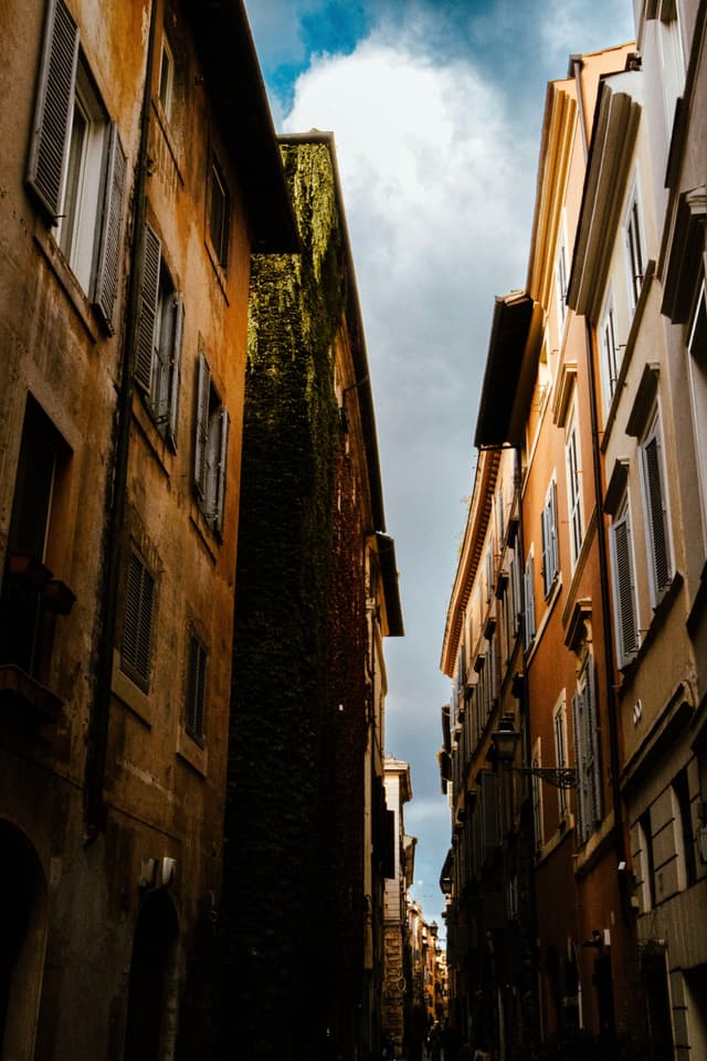 A narrow alleyway between tall, closely packed buildings with a partly cloudy sky above
