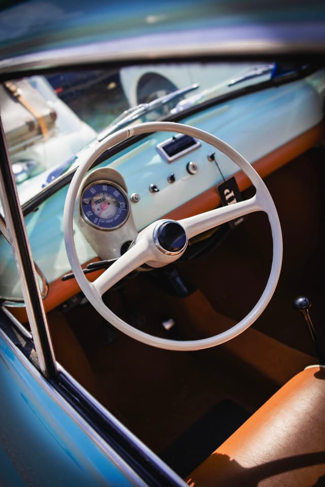 A vintage car interior featuring a white steering wheel, a classic speedometer, and brown upholstery
