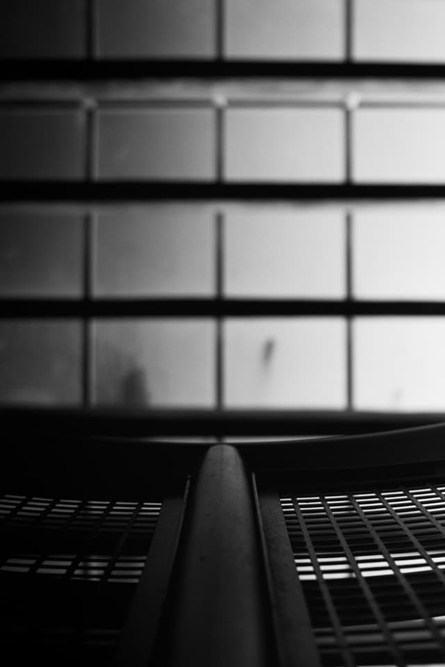 A black and white abstract composition featuring a grid-like pattern in the foreground and a blurred, tiled background