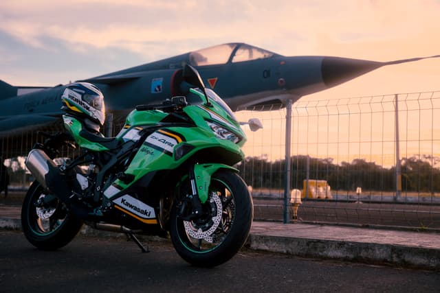 Green motorcycle parked in front of a fighter jet with a sunset backdrop