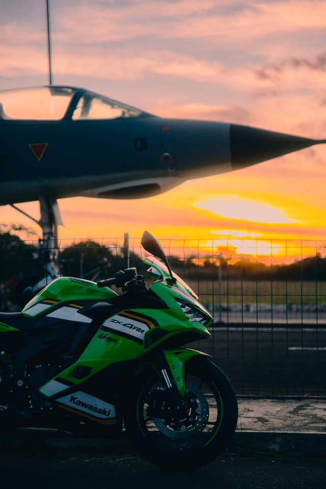 Green motorcycle parked in front of a jet at sunset