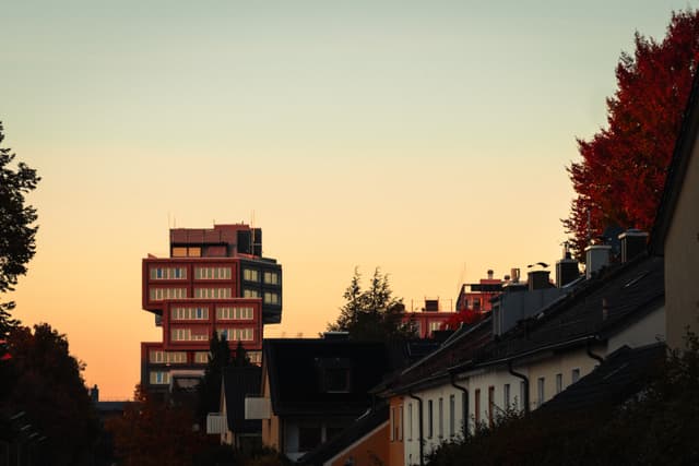Urban skyline with a modern building and traditional houses under a sunset sky