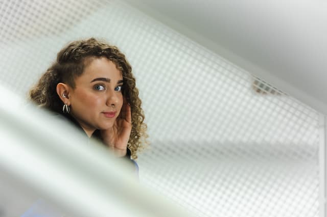 A person with curly hair and earrings is looking over their shoulder, framed by a geometric pattern in the foreground
