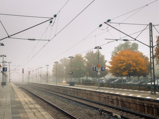 Empty train platform with overhead wires and autumn trees in foggy weather