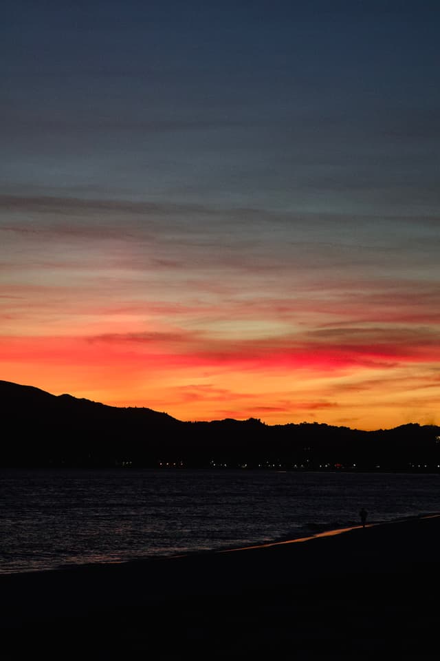 A vibrant sunset over a calm sea with silhouetted mountains and a colorful sky transitioning from deep blue to orange and pink hues