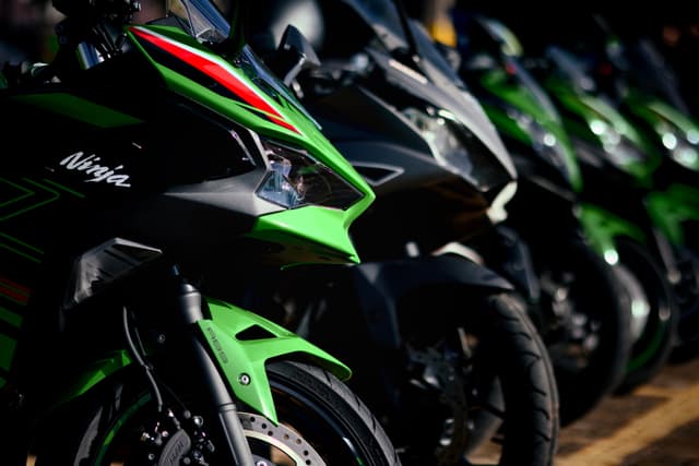 A row of green and black sport motorcycles parked closely together, with a focus on the front sections