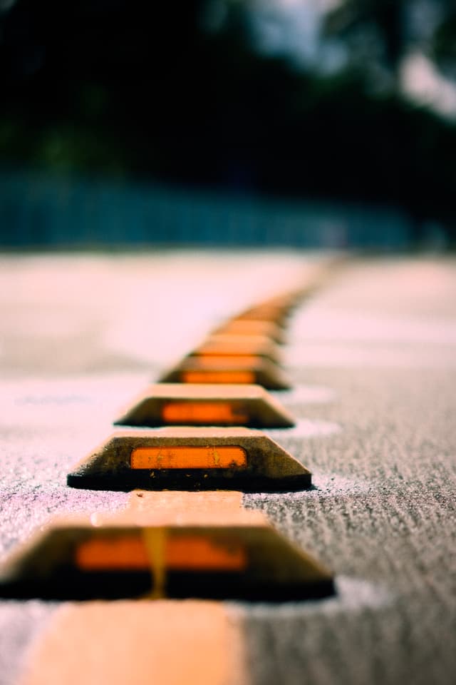 A close-up of reflective road markers on a street, with a shallow depth of field and a blurred background