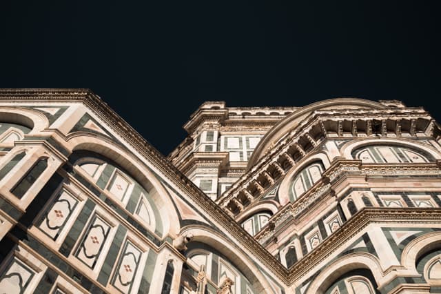 Upward view of an ornate cathedral exterior with arched windows and geometric marble detailing against a dark night sky