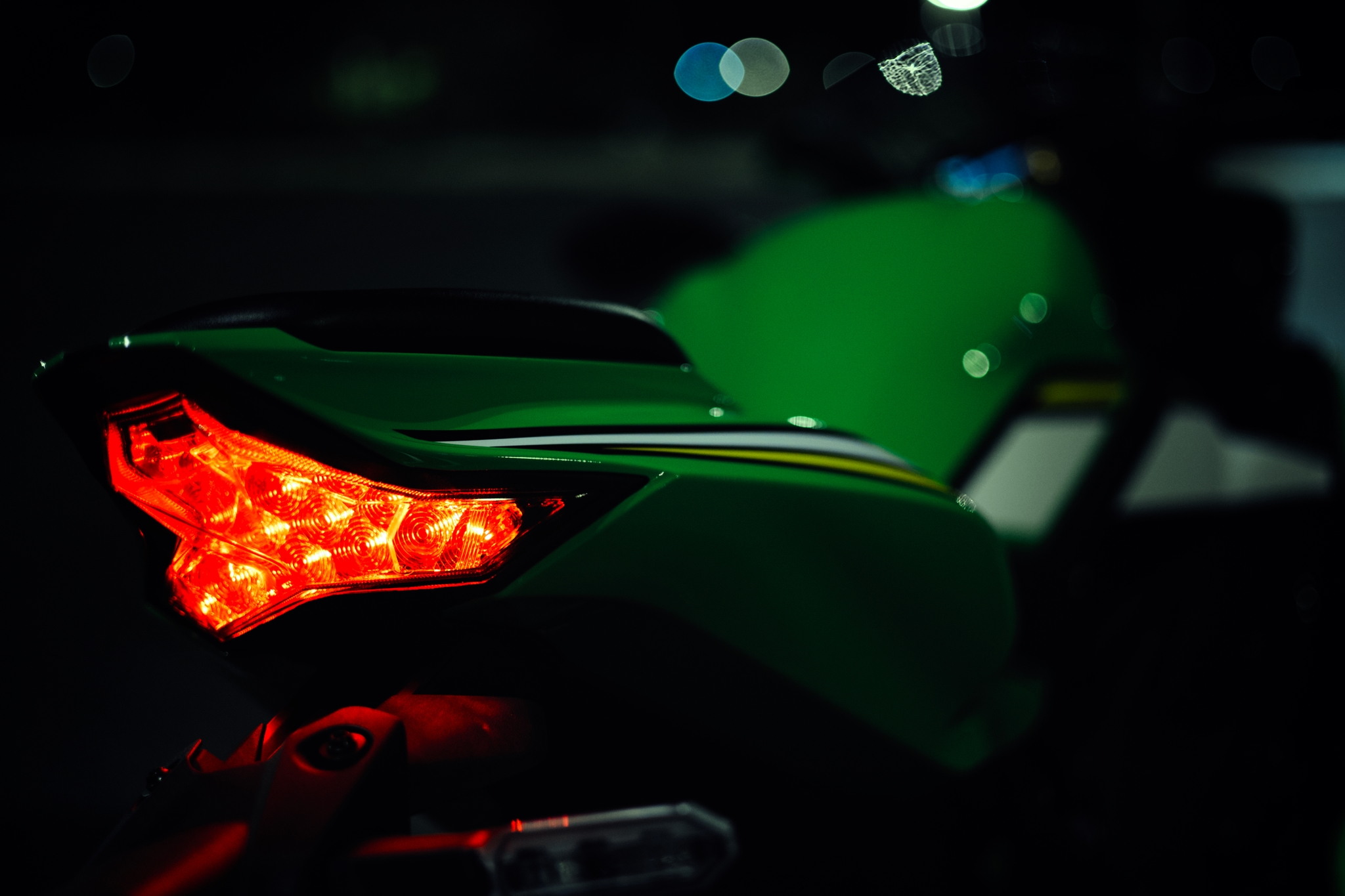Illuminated motorcycle taillight at night with a vibrant green body and distinct red light