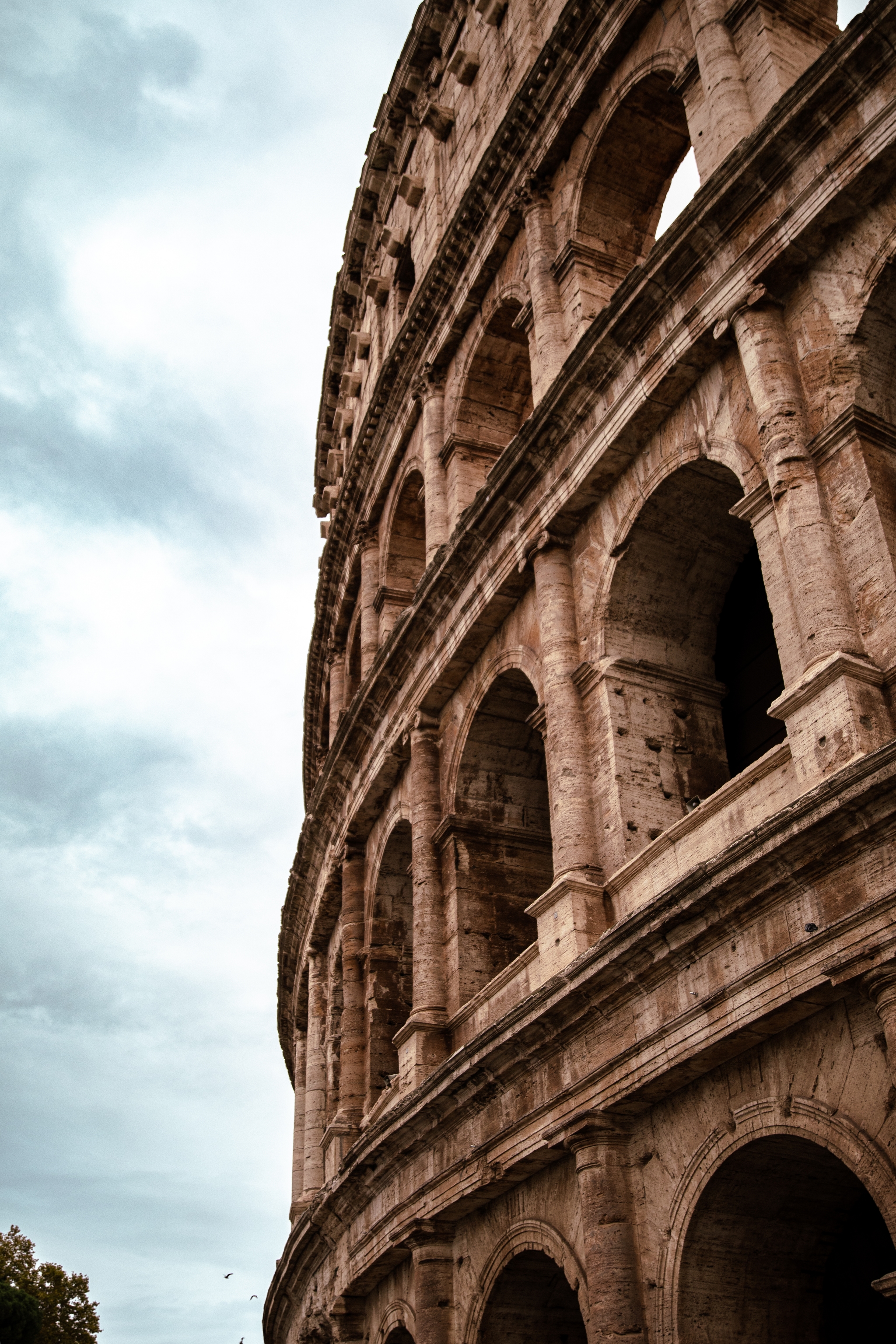 Upward view of the Roman Colosseum’s stone arcades against a cloudy sky