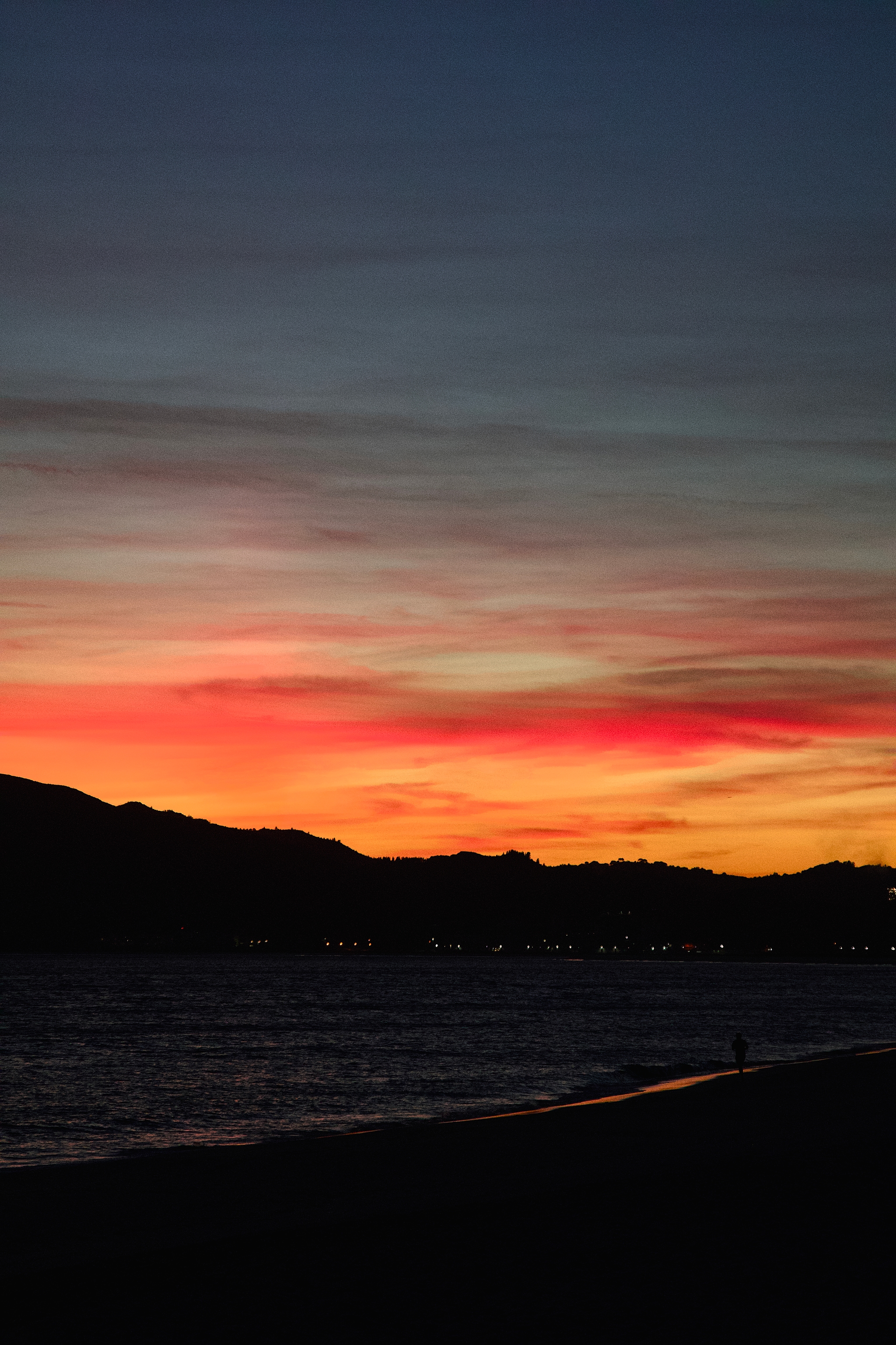 A vibrant sunset over a calm sea with silhouetted mountains and a colorful sky transitioning from deep blue to orange and pink hues